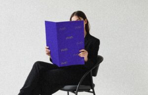 Woman seated, dressed in black, holding a large purple folder that says "push".