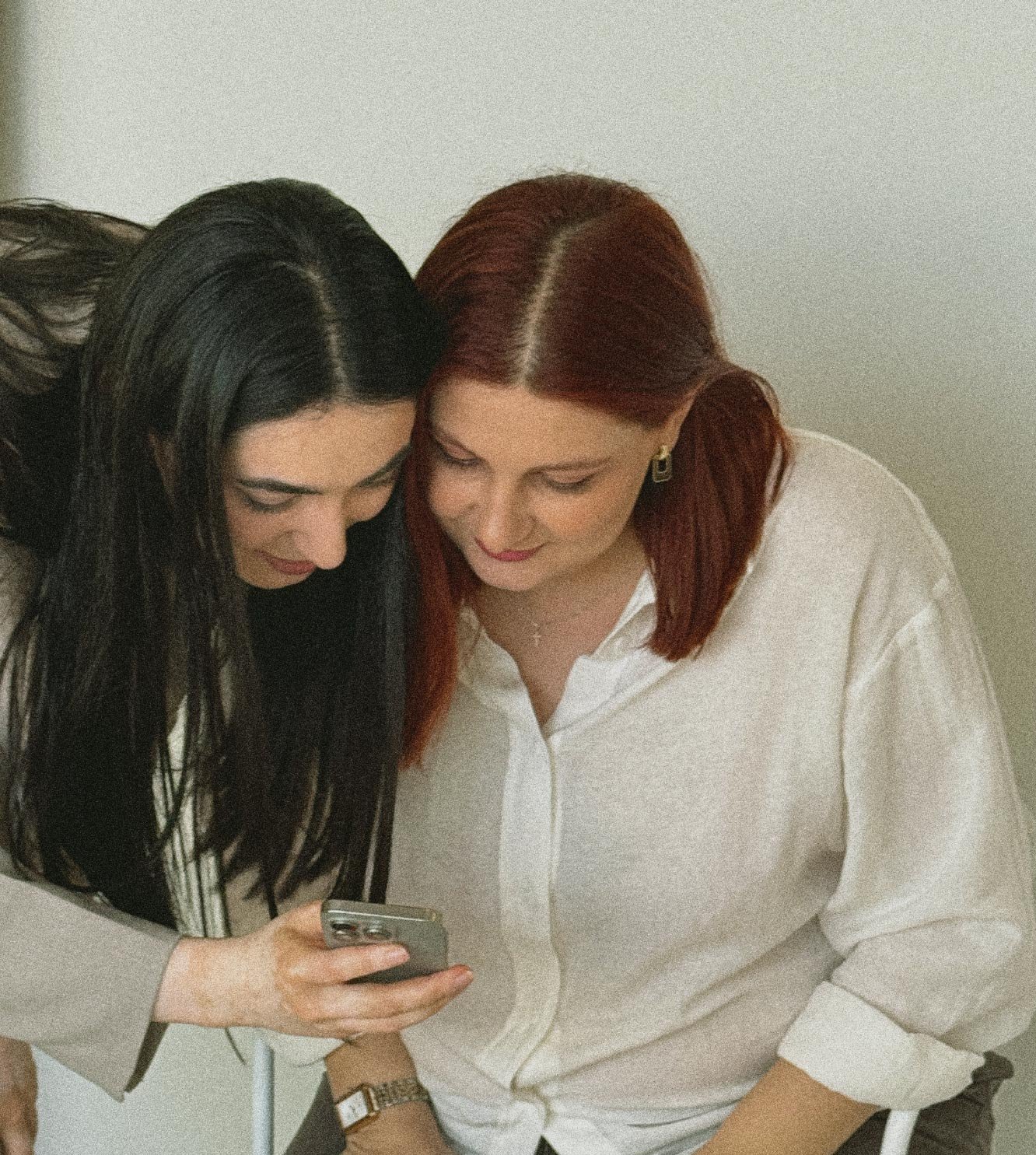 Two women looking at a smartphone together and smiling.